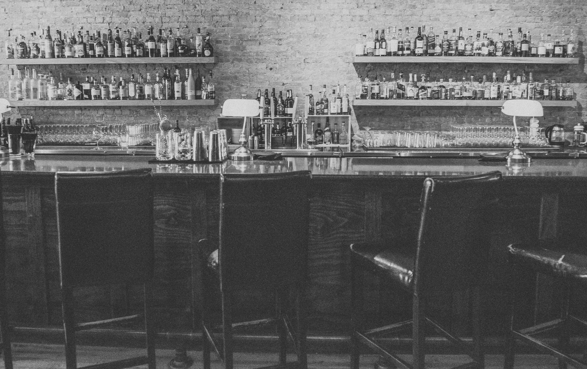 Bar interior with shelves of liquor bottles behind a counter and glassware in front.